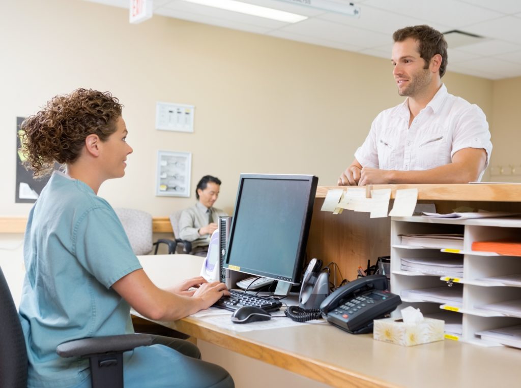 front office staff member talking to a patient while at the desk wearing scrubs after completing dental front office training