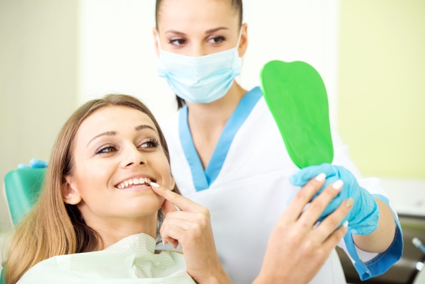 female dental patient pointing to tooth in mirror while dentist stands behind her wearing a mask happy that her dental marketing strategies have worked to attract the new patient she wanted